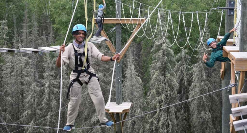 two students are suspended by ropes as they make their way through a ropes course on an outward bound expedition